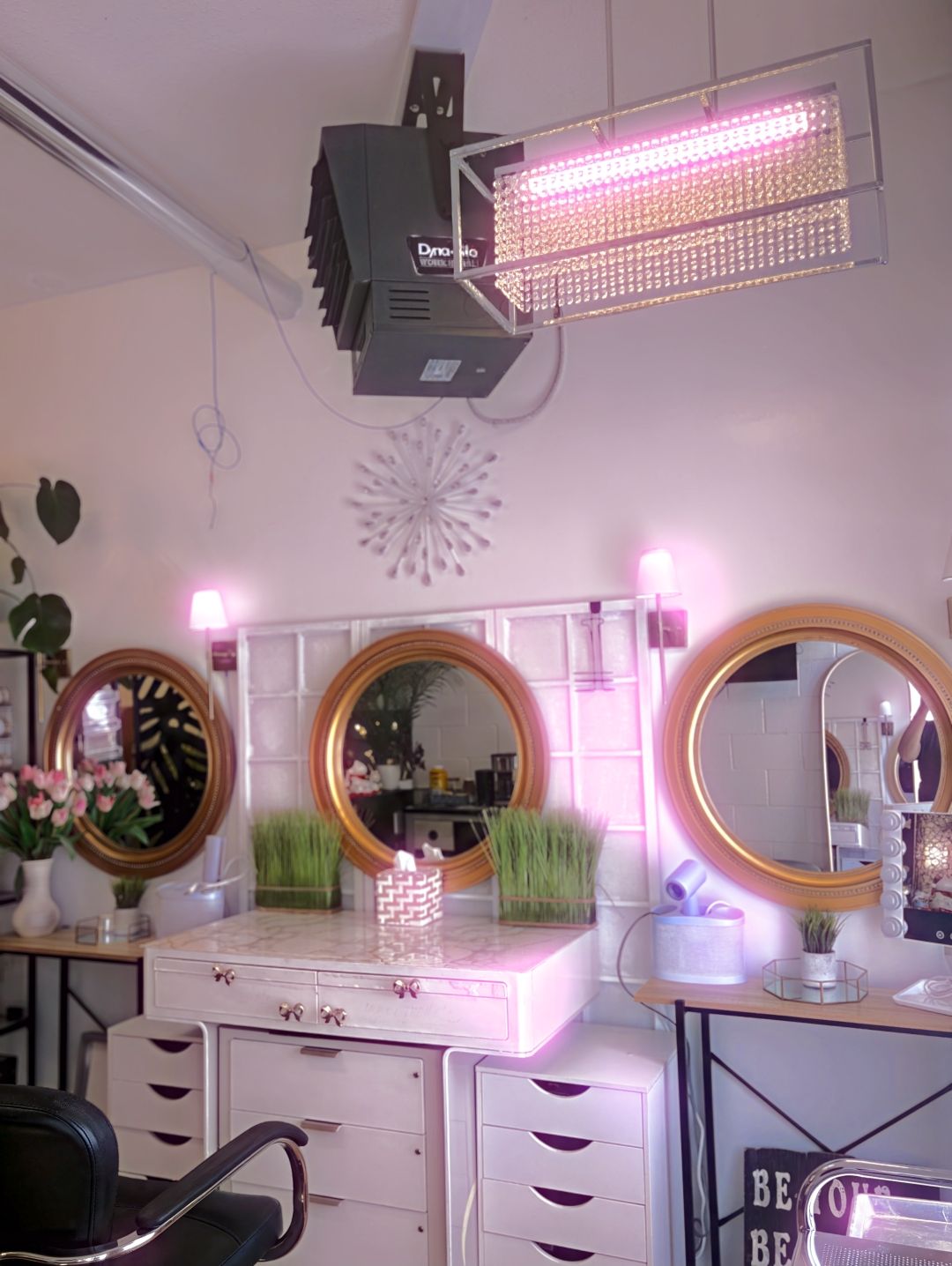 Three round gold mirrors over a white vanity in pink light